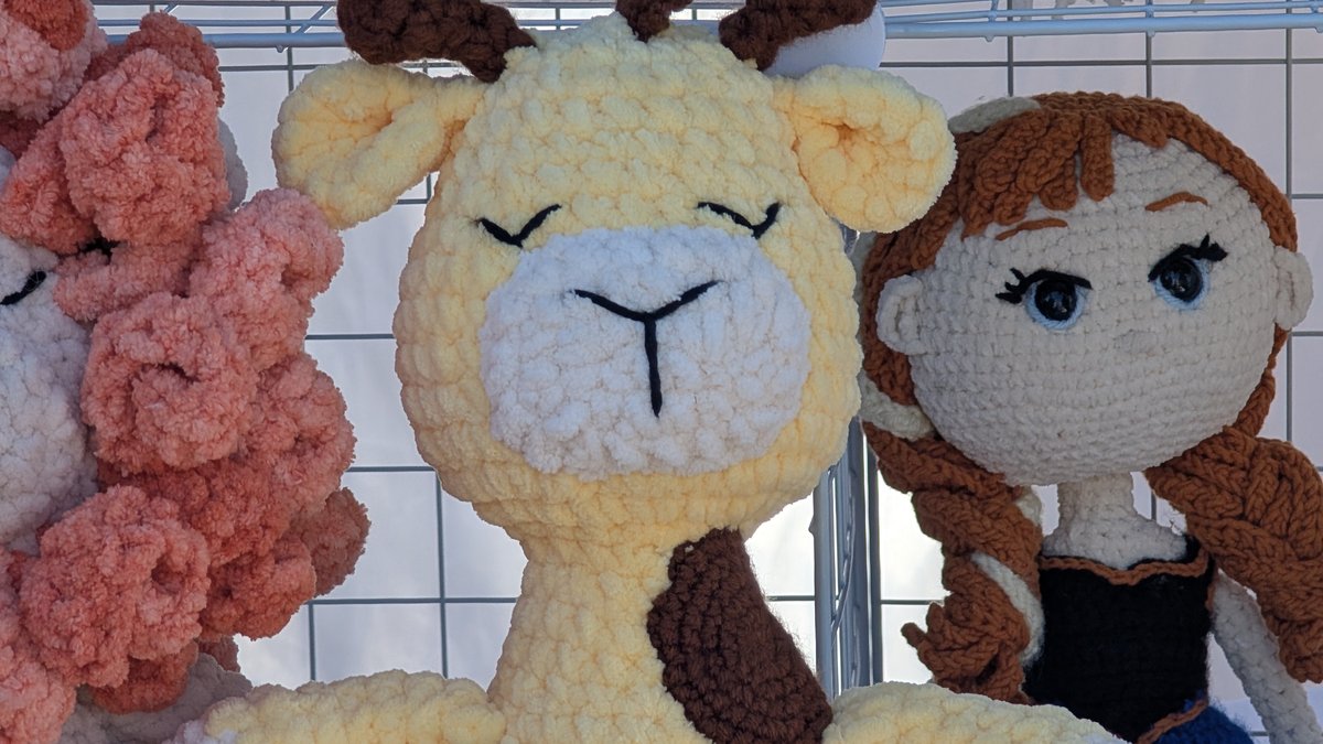 Large chenille crochet plush toys in cream and pink on a craft fair display rack