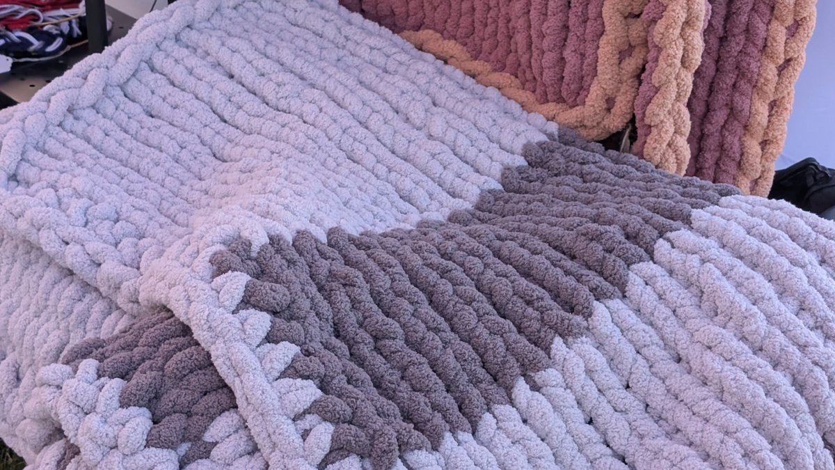 Chunky chenille blankets in grey, cream and dusty rose folded on a craft fair table