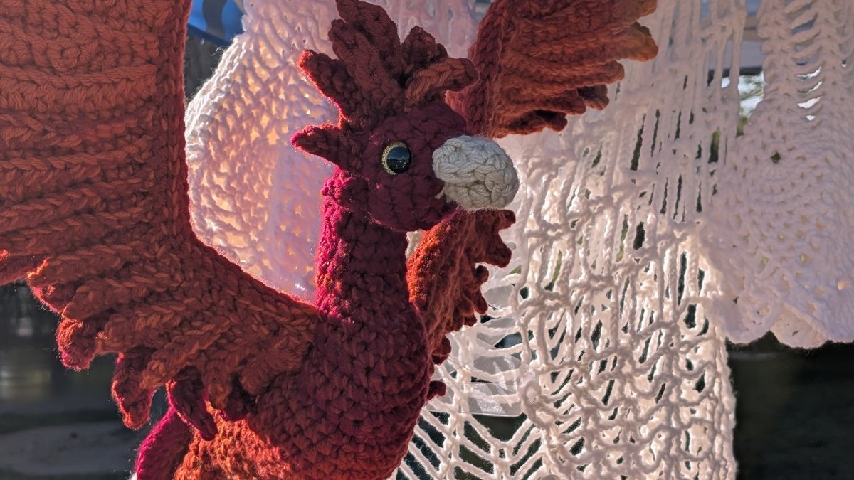 A crocheted phoenix in deep red and orange yarn with outstretched wings, displayed at a craft fair